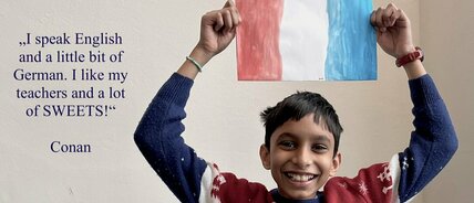 Ein Junge lacht und hält eine französische Flagge in den Händen.